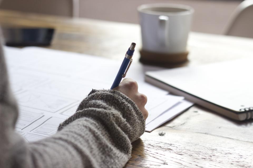 Hand writing notes with a pen next to a cup of coffee