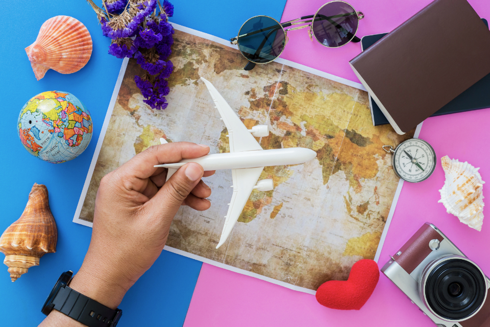 Hand holding a toy airplane over a world map with travel items